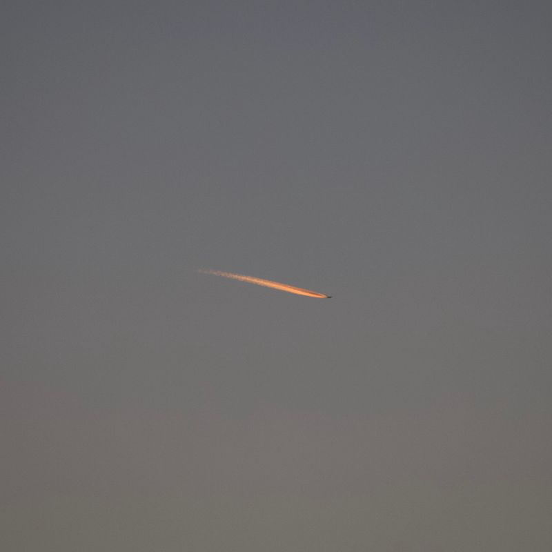 an airplane in the sky, lit up by the sunset